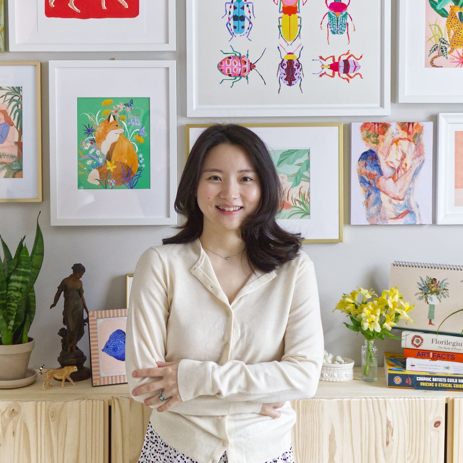 Portrait of Sun Lee in her art studio, smiling gently. Behind her, the walls are decorated with her own colorful, nature-inspired artwork, creating a vibrant and personal backdrop that reflects her creative world.