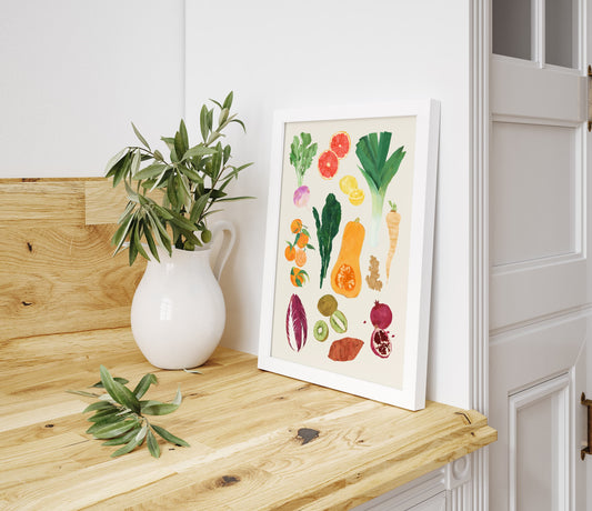 Framed artwork of colorful vegetables on a wooden surface with a plant and pitcher.