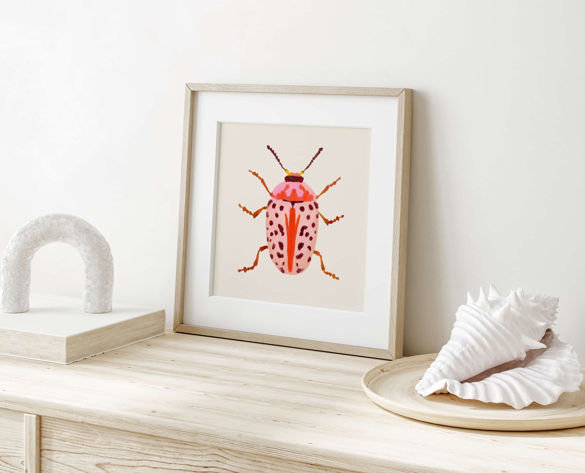 Gouache painting of a blush-colored beetle with coral and baby pink tones, accented with wine-maroon dots and curving tentacle-like antennae. A soft yet striking insect illustration.