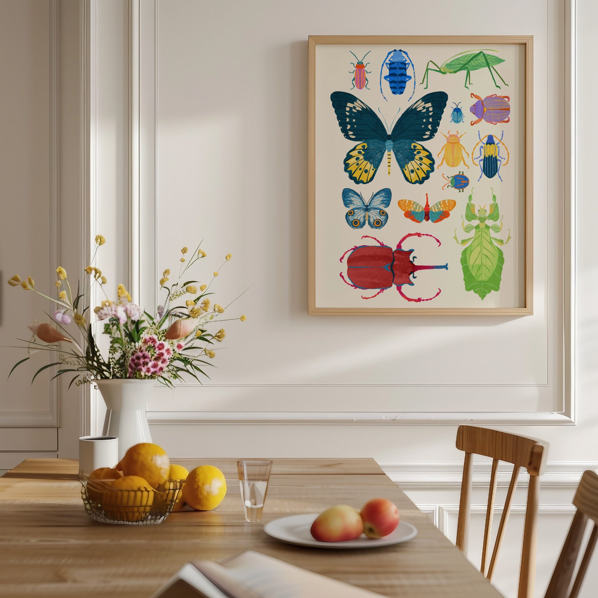 Dining room with a framed illustration of colorful insects on the wall, a table with fruit and flowers, and chairs.