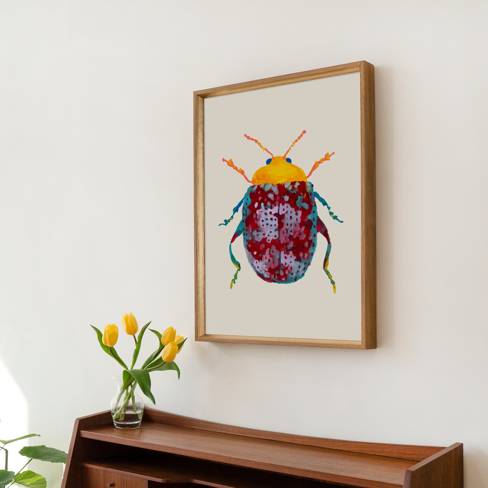 Framed artwork of a colorful beetle on a wall above a wooden shelf with flowers.