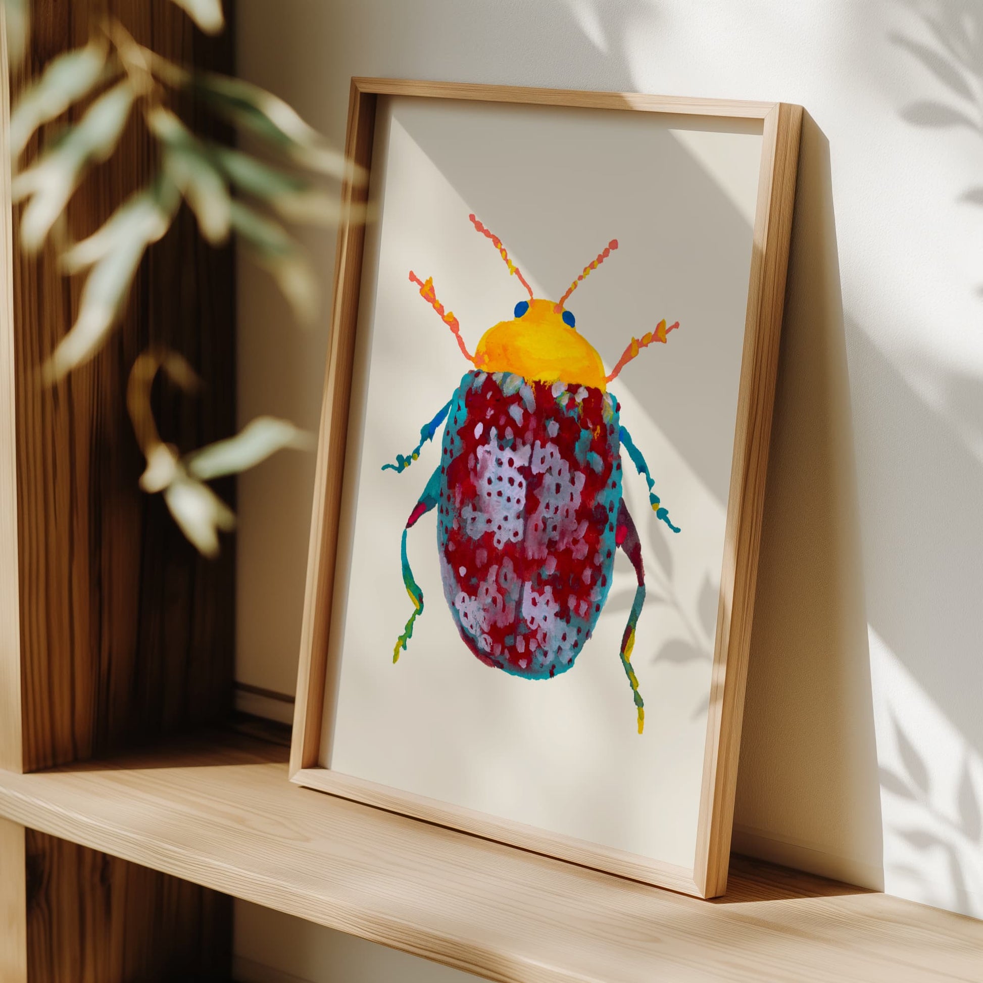 Framed artwork of a colorful beetle on a wooden shelf with a plant in the background