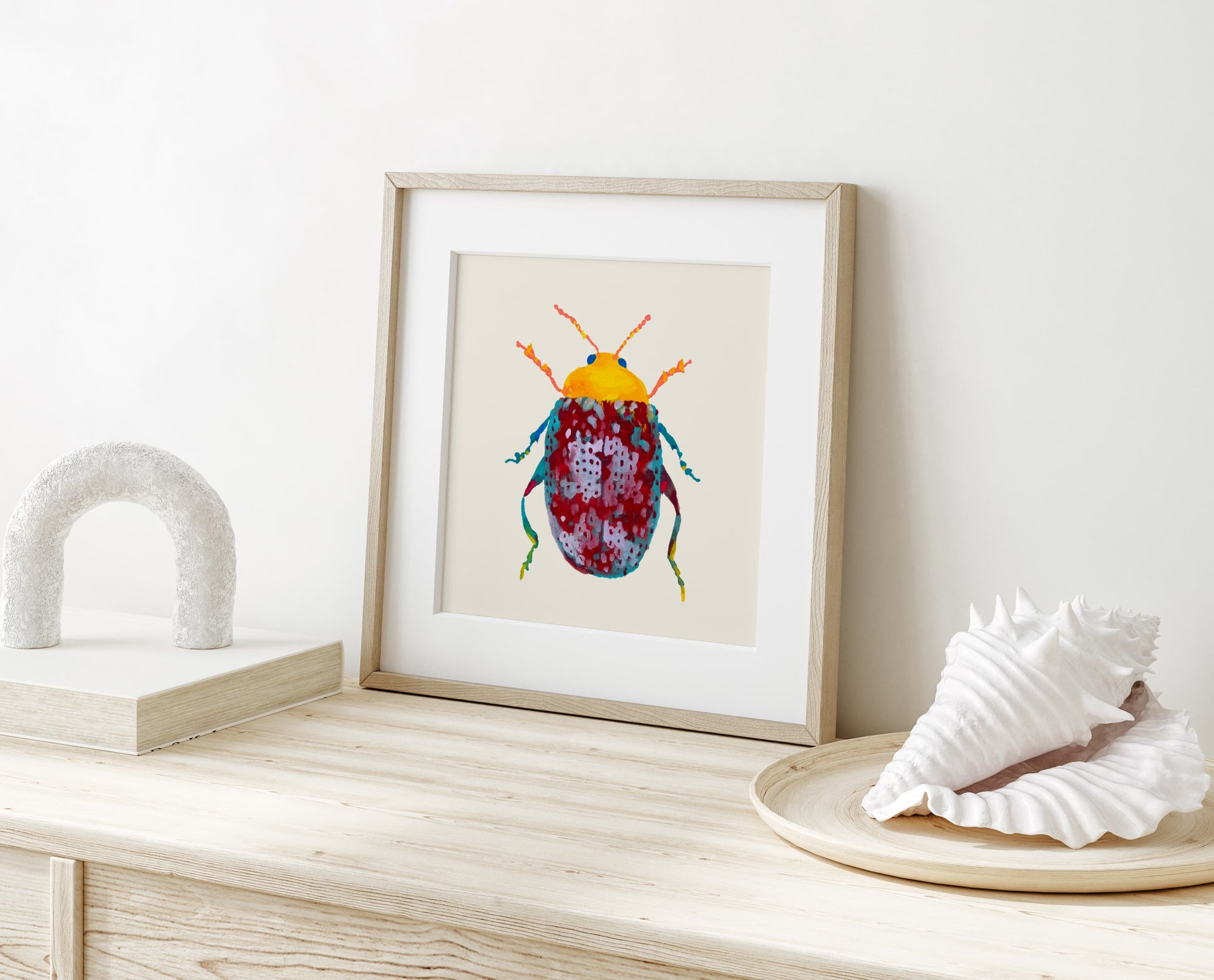 Framed artwork of a colorful beetle on a wooden surface with decorative shells.