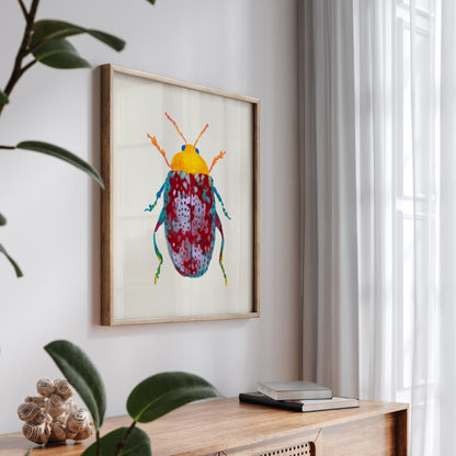 Colorful beetle artwork in a wooden frame on a wall above a wooden surface with books and a plant.
