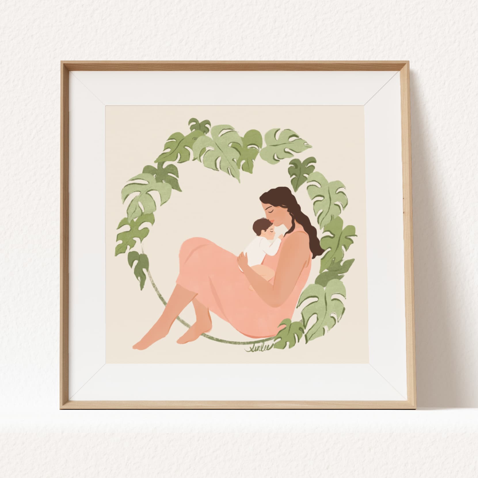Framed artwork of a mother and child surrounded by green leaves on a beige background